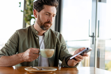Businessman drinking coffee and using smartphone in cafe