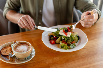 Man eating fresh salad with feta cheese in restaurant