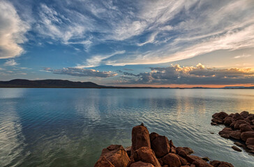 landscape over water at the lake dam at sunset with hills and rocks, blue sky with clouds, Africa Botswana