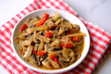champignon mushrooms, onions, and red bell peppers cooked with black pepper in a white ceramic dish.