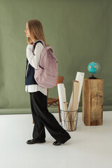 Side view of student girl with backpack standing near school props, including globe and rolled papers, symbolizing education and learning concept