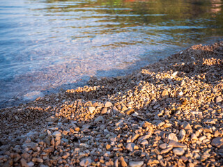 Pebble beach with small limestone stones and clear Adriatic Sea water, photographed in Croatia, showing typical Mediterranean coastal shoreline.
