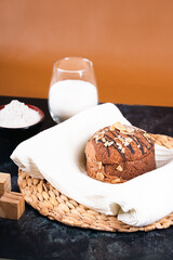 A round chocolate bread topped with almond slices, placed on a white cloth over a woven mat, surrounded by simple props on a dark background.