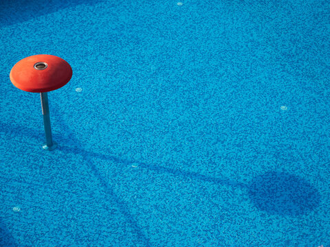 Detail of empty swimming pool with blue mosaic tiles and red water fountain structure casting a shadow.
- Powered by Adobe