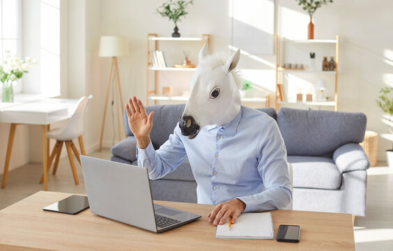 Businessman wearing horse mask joins online video call at home, working with laptop for meeting and conversation, ensuring business communication in a unique and quirky setting with focus.