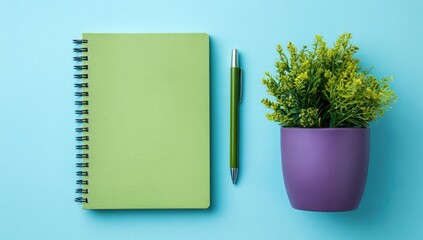 Pastel green spiral notebook, purple pot plant, and green pen on a light blue surface