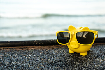 Vacation savings concept with piggy bank wearing sunglasses and beach umbrella. Piggy bank on...