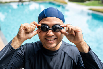 A person in a dark swim cap and rash guard adjusts their swimming goggles ready to dive into the pool. Aquatic sports and a healthy active lifestyle perfect fitness and summer activities.