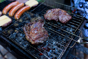 steaks are grilled and shot with selective focus, with hamburger patties and sausages being prepared in the background