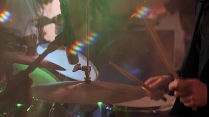 A musician plays a drum kit with sticks, hands in close-up. A dynamic drummer skillfully plays the drums to the rhythm of a live concert performance.