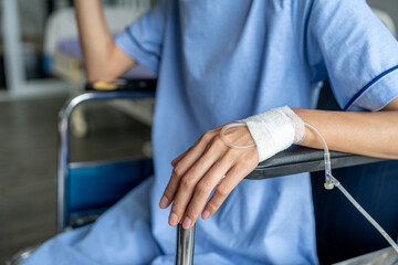 A cancer patient sits in a wheelchair with an IV drip looking stressed and sad. Asian Woman receiving IV therapy in a wheelchair showing visible signs of stress and depression