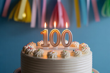 Close up of 100th birthday cake with flickering candle. Celebration of longevity and reaching a century of life