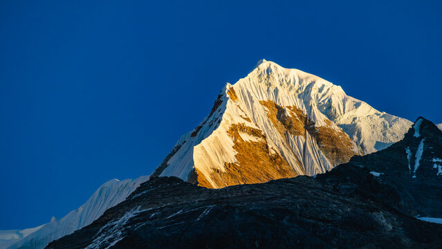 Snow clad himalayan mountain peak of singu chuli glowing in golden sunlight against blue sky in Annapurna sanctuary region in nepal