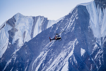 Helicopter flying through snow capped himalayan mountain range for rescue, transportation, tour.