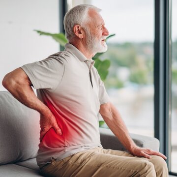 An elderly man is experiencing pain in his lower back, highlighted by a red area on his side.