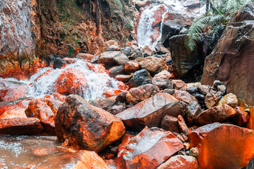 A scenic sulfur-rich stream with orange rocks and a waterfall in tropical nature. Perfect for concepts of geology, volcanic activity, hot spring, minerals, and natural landscape.
