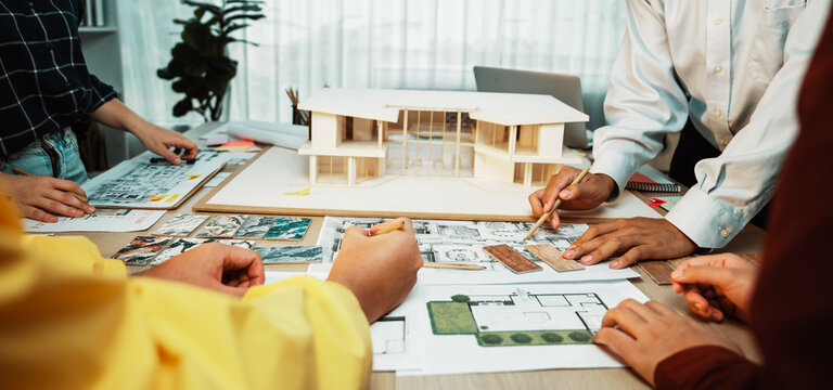A diverse team collaborates on architecture designs, focusing on models and detailed sketches. The modern workspace inspires creativity and teamwork in planning. SACTR - Powered by Adobe