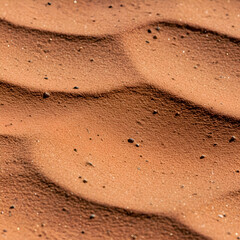 Red desert sand with small pebbles, exhibiting rippled texture. Close-up view of natural formation in a desert landscape.