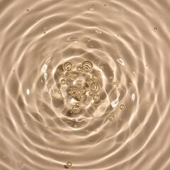 Abstract image of light beige liquid with concentric ripples and various sized bubbles. Close-up view of the liquid's texture and surface tension.