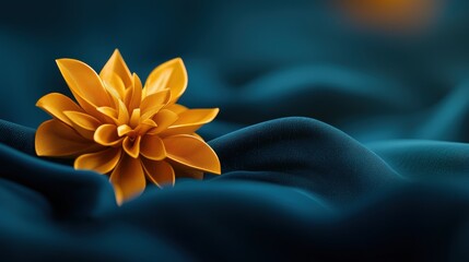 A single orange flower with six petals rests on a dark blue fabric.