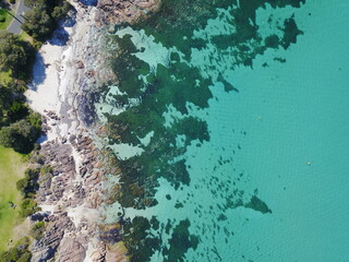 Aerial view of Dunsborough, Western Australia, showcasing clear turquoise waters, rocky shoreline, and white sandy beach. Vibrant coastal scenery contrasts lush greenery with the sparkling Indian Ocea