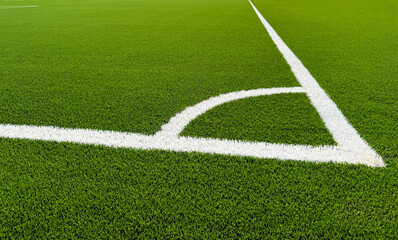 Fototapeta premium The football field corner with artificial green grass. Line in corner area of soccer field. Photo of a green synthetic grass sports field with white line shot from above. Football grass field corner.