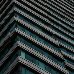 Obraz premium Modern skyscraper facade with numerous windows in a teal tint. Geometric design of the building's structure with a gray stone exterior.