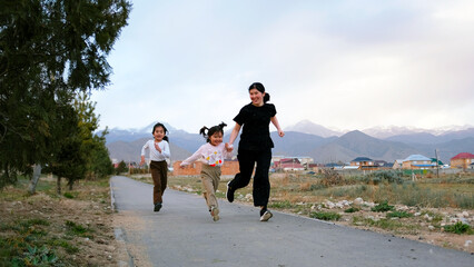 A woman and two children are running along a path in the park. A mother holds her youngest daughter's hand while jogging in the fresh air
