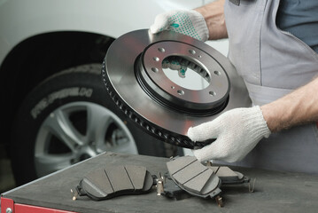 An auto mechanic prepares the replacement of the brake disc and brake pads. On the desktop, an auto mechanic inspects and controls spare parts-a new brake disc and a set of brake pads. © Jevgenyij