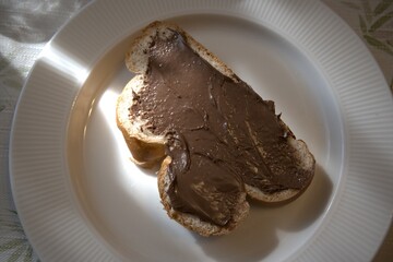A single slice of sweet bread topped with creamy hazelnut spread served on a white plate with hand in natural morning light. Concept of breakfast, comfort food, and homemade sweetness.
