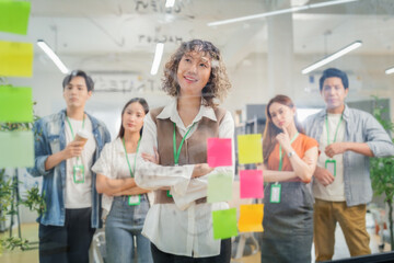 Asian business creative marketing team brainstorming startup strategy using glassboard and sticky notes. Collaborative ideation session demonstrates design thinking methodology disruptive innovation