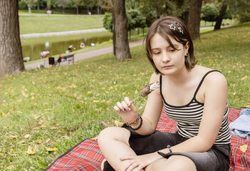 Young Girl Enjoys a Sweet Treat While Sitting on a Blanket in a Peaceful Park Surrounded by Nature on a Sunny Afternoon