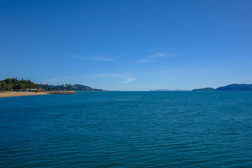 Fototapeta premium Scenic coastal view from Townsville pier, Queensland, with turquoise waters, distant islands, and clear blue sky. Perfect for travel, tourism, tropical nature, and landscape themes.
