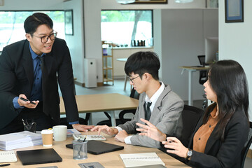 A group of people are sitting around a table in a business setting. One man is standing and talking to the group.