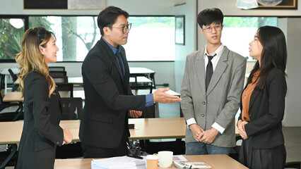 A group of people are stand around a table in a business setting. They are dressed in business attire and appear to be discussing something important