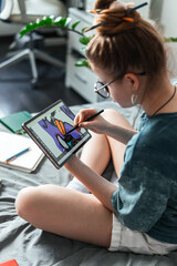 Girl practices digital art using tablet while studying at home. Illustration learning, freelance development and self-expression through creative technology in modern cozy environment