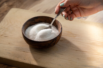 Granulated sugar filled in wooden bowl and hand with a spoon. Close up view of white sugar