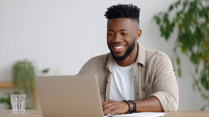 Young African American man laughing while working on laptop at home office desk