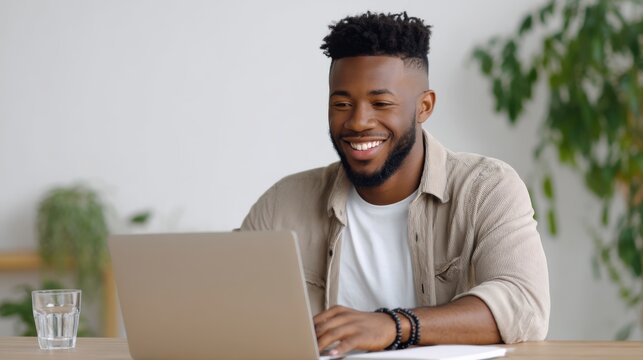 Young African American man laughing while working on laptop at home office desk