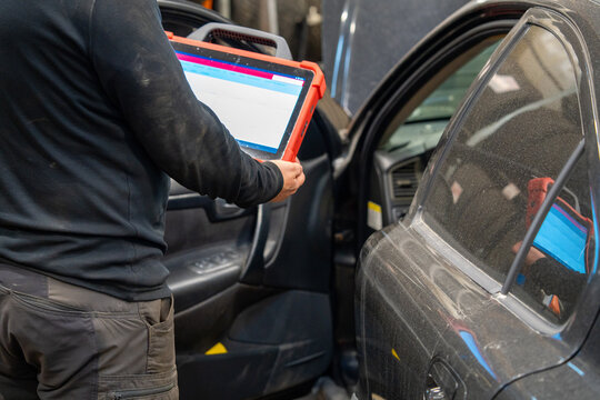 A Car diagnostic specialist using an electronic tablet scanner in an automotive repair garage. Mechanic performing vehicle computer system analysis with professional diagnostic equipment