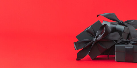 Elegantly wrapped black gifts with black ribbons and bows on a wide red background symbolizing the celebration and sale of Black Friday.