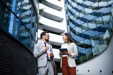 Businesspeople talking and holding a coffee and a tablet in front of office buildings