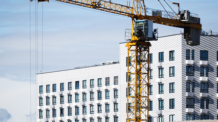 Yellow tower crane working on construction site near a modern high-rise residential building with many windows, urban development concept   © belavinstock