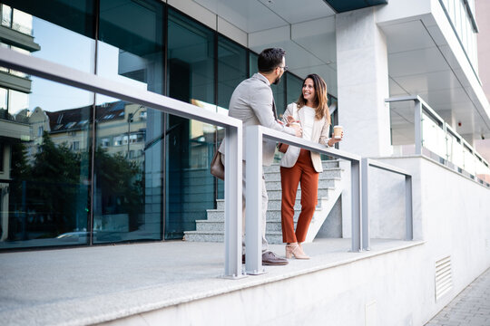 Business colleagues enjoying coffee break while chatting outside office building