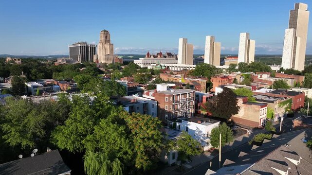 Row homes and two-story houses in red brick style in front of downtown skyline. Sunny day with blue sky in Albany, New York. Aerial wide shot. New York State capitol and Empire State plaza in back.