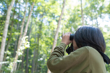 森の中で双眼鏡を構えて野鳥観察をする若者