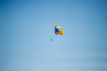 A person parasails beneath a vibrant rainbow-colored parachute, soaring high in a clear blue sky.