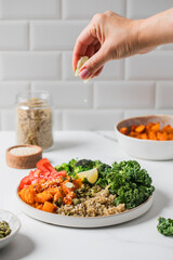 A woman's hand squeezes lime juice onto a healthy vegan Buddha bowl with quinoa, baked vegetables. 