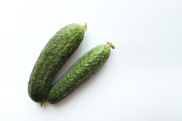 Two fresh cucumbers lie on a clean white surface, highlighting their smooth skin and vibrant green color. The fresh produce looks crisp and ready for various culinary uses.