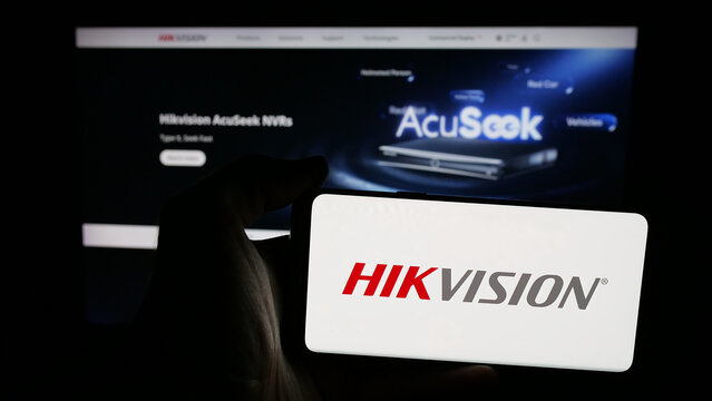 Stuttgart, Germany - 08-22-2025: Person holding mobile phone with logo of Hangzhou Hikvision Digital Technology on screen in front of web page. Focus on phone display.